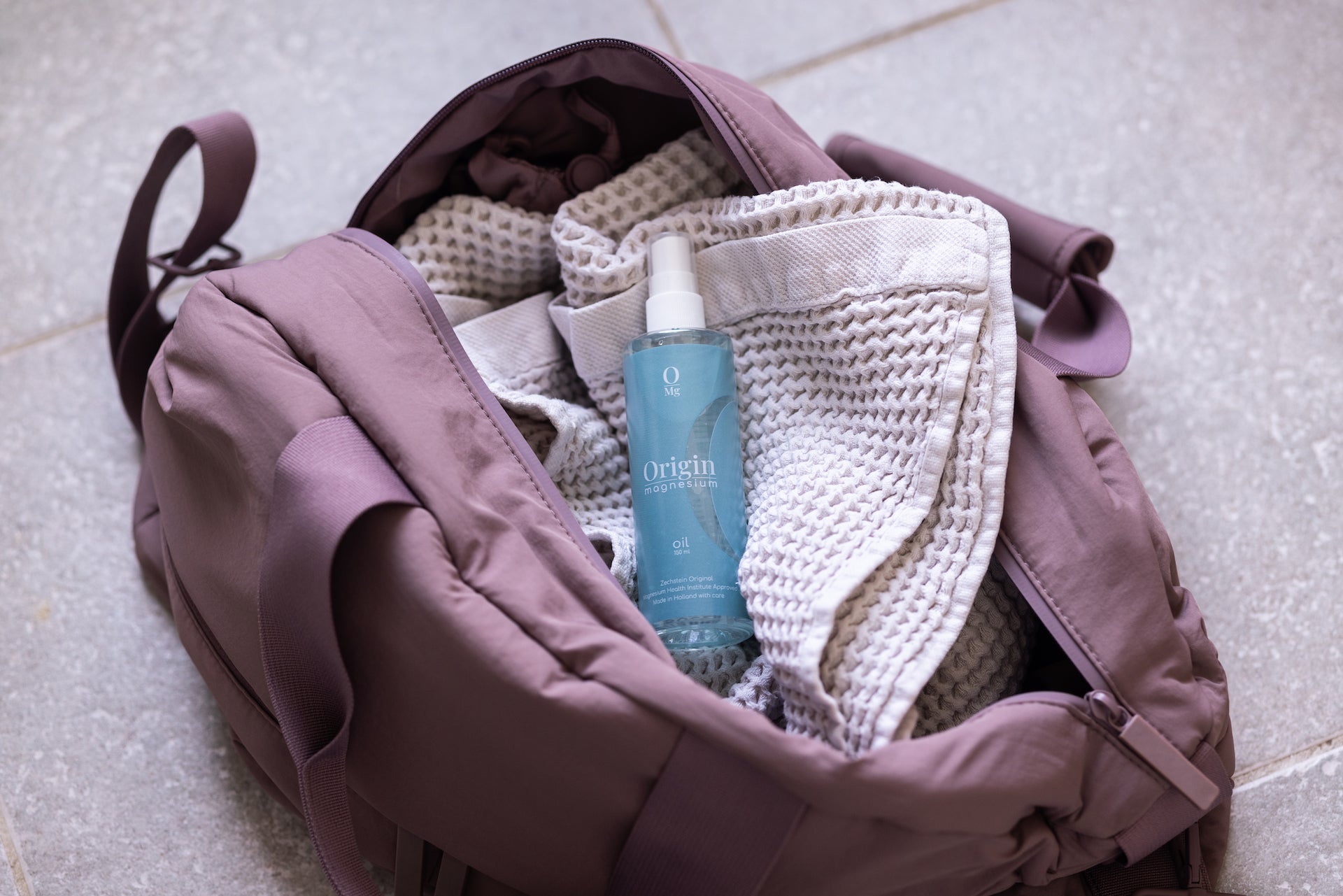 Weekend bag with towel with origin magnesium oil on top in blue bottle